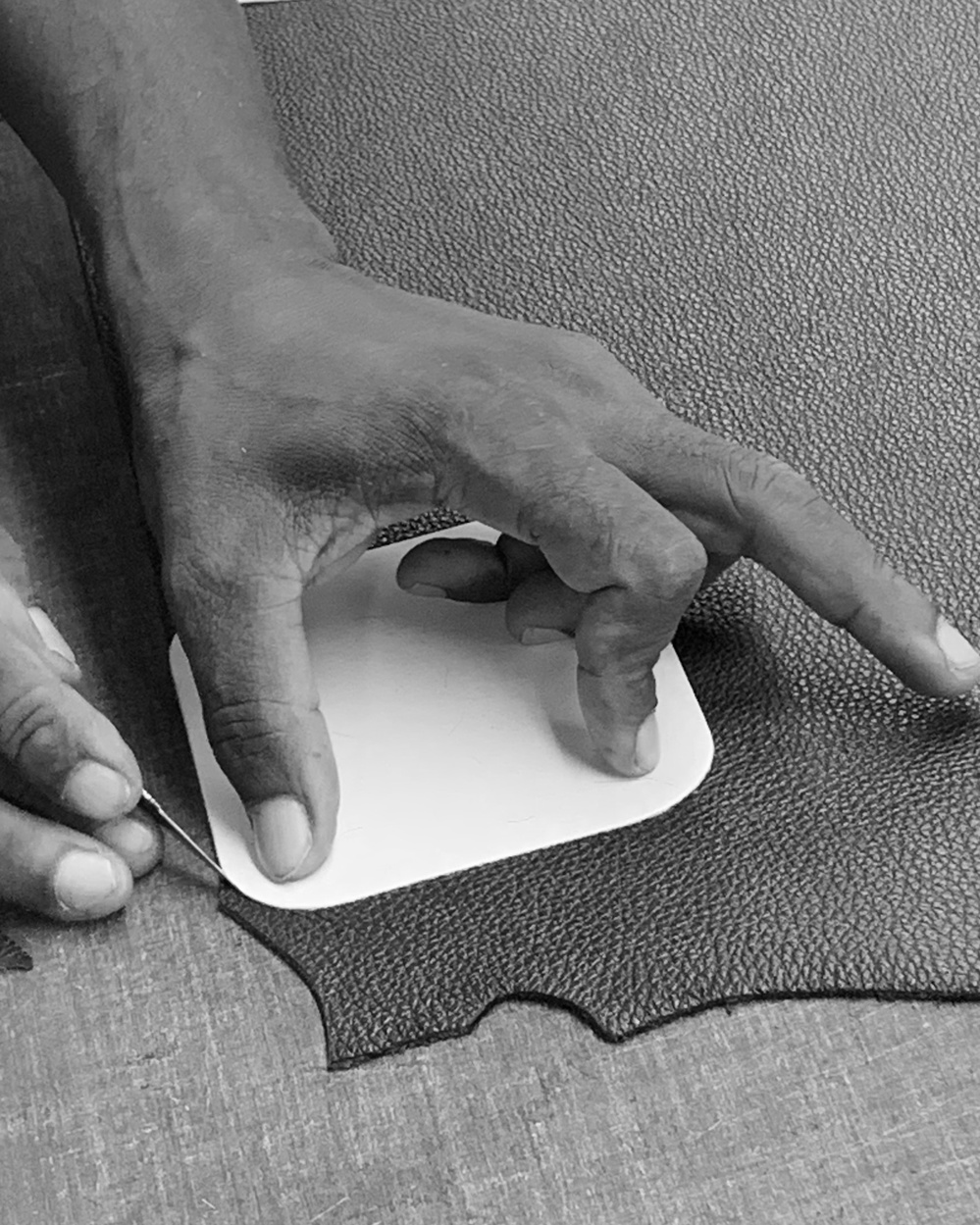 A black & white image of a master craftsman cutting leather to size.