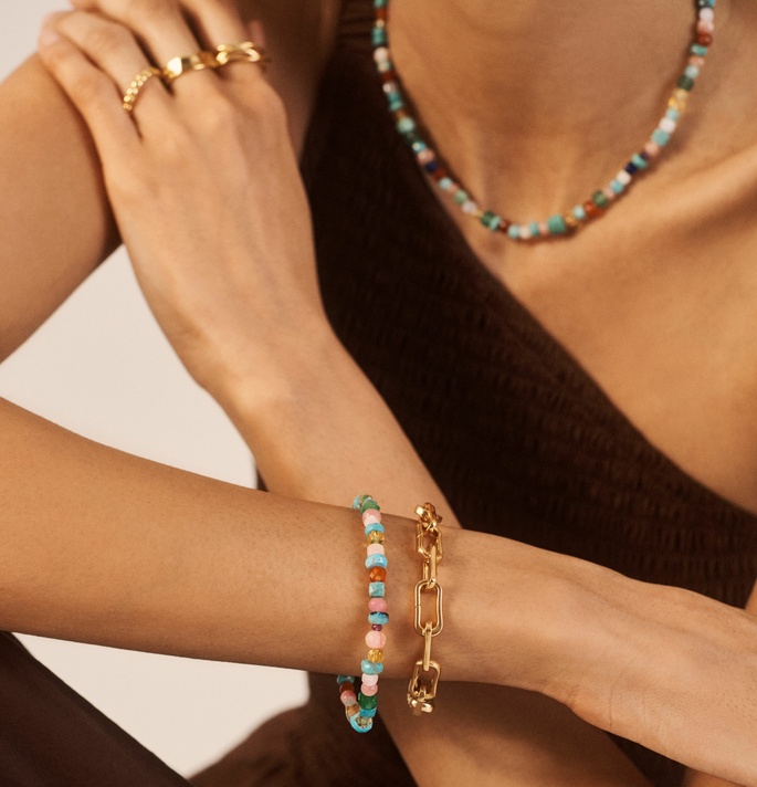 A model in a dark top wearing a gemstone bracelet, Alta Capture Charm Bracelet and gold rings