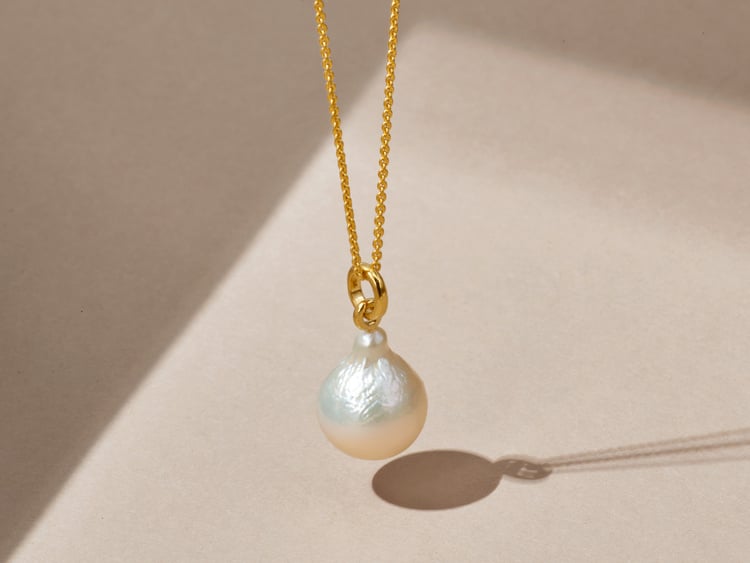 A pearl hanging from a delicate gold chain